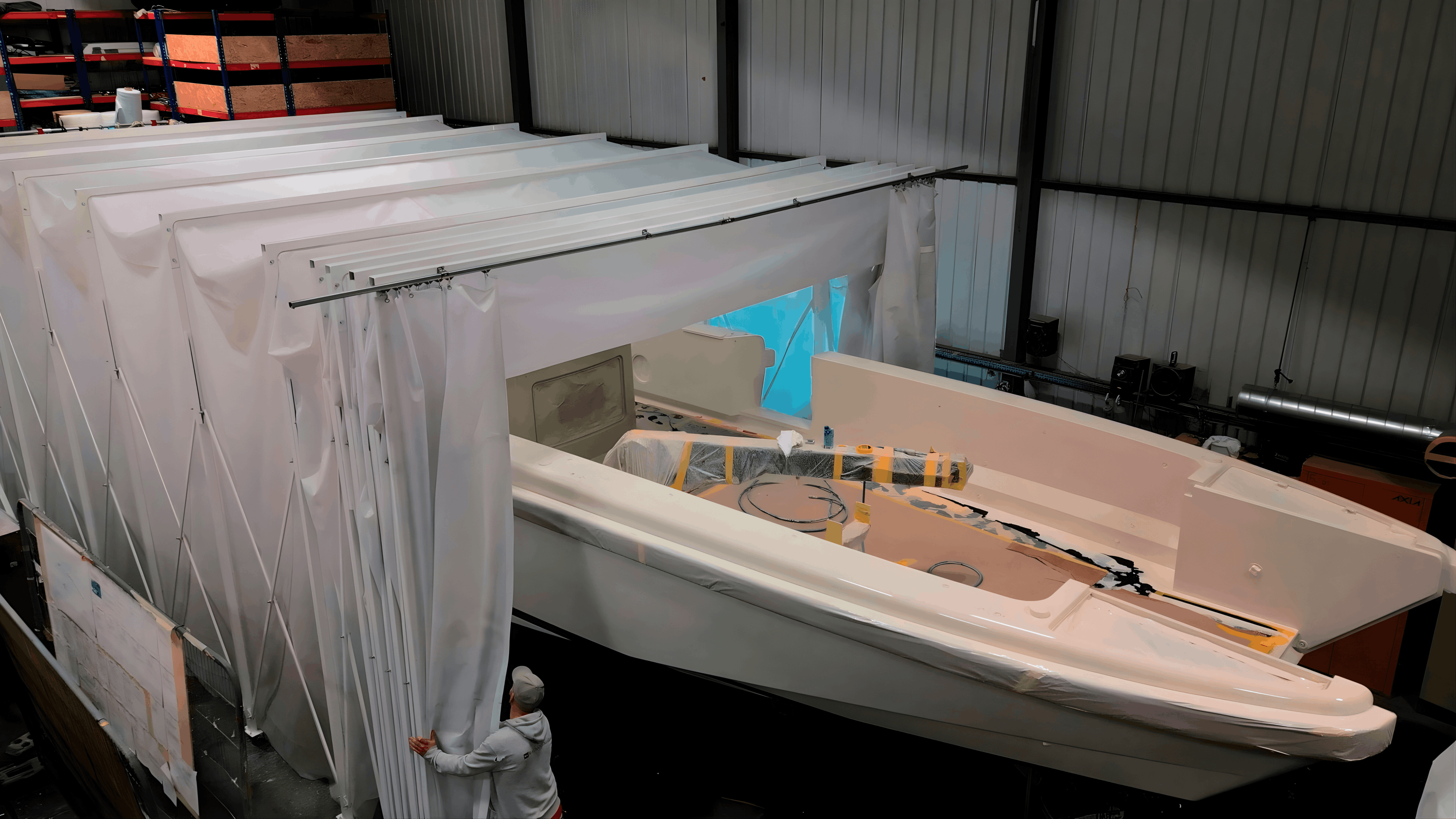 Retractable spray booth installed alongside a yacht hull, with curtain panels being drawn back to allow access.