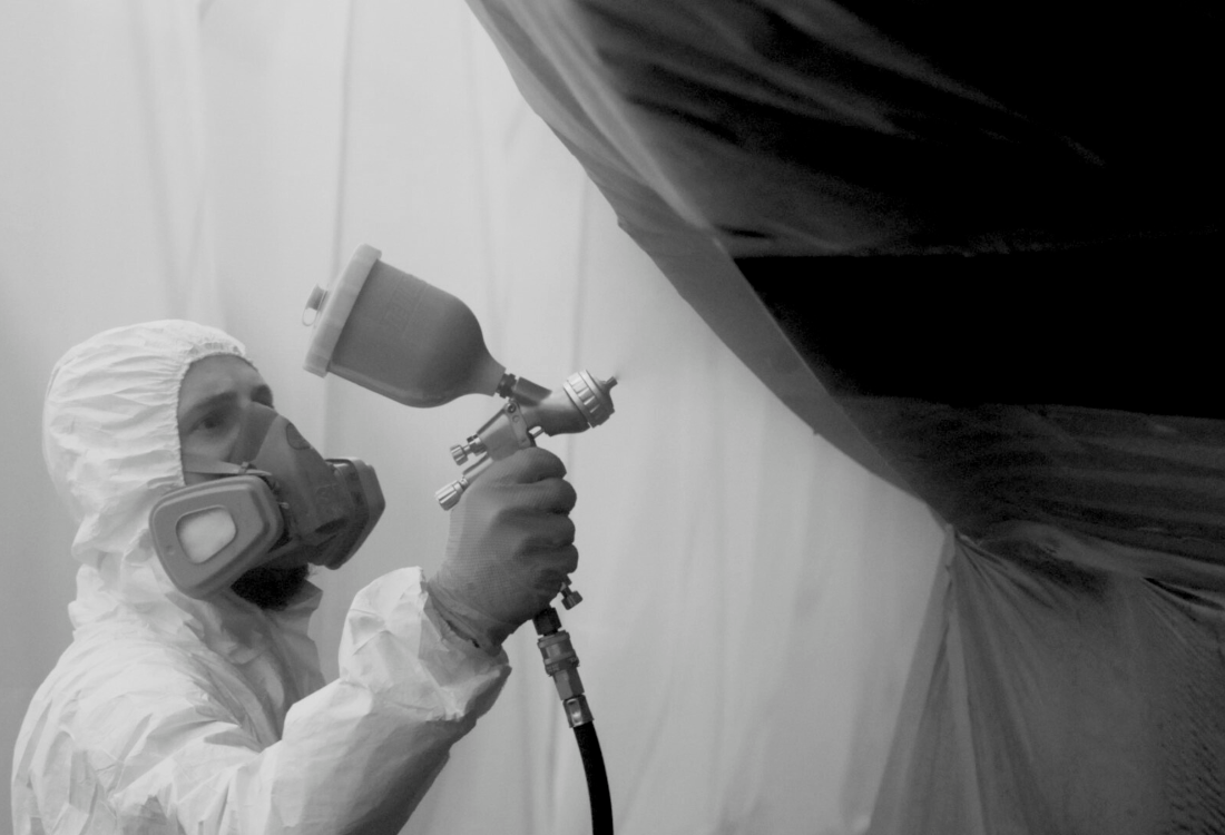 Operative using a spray gun inside a retractable spray booth during super yacht maintenance.