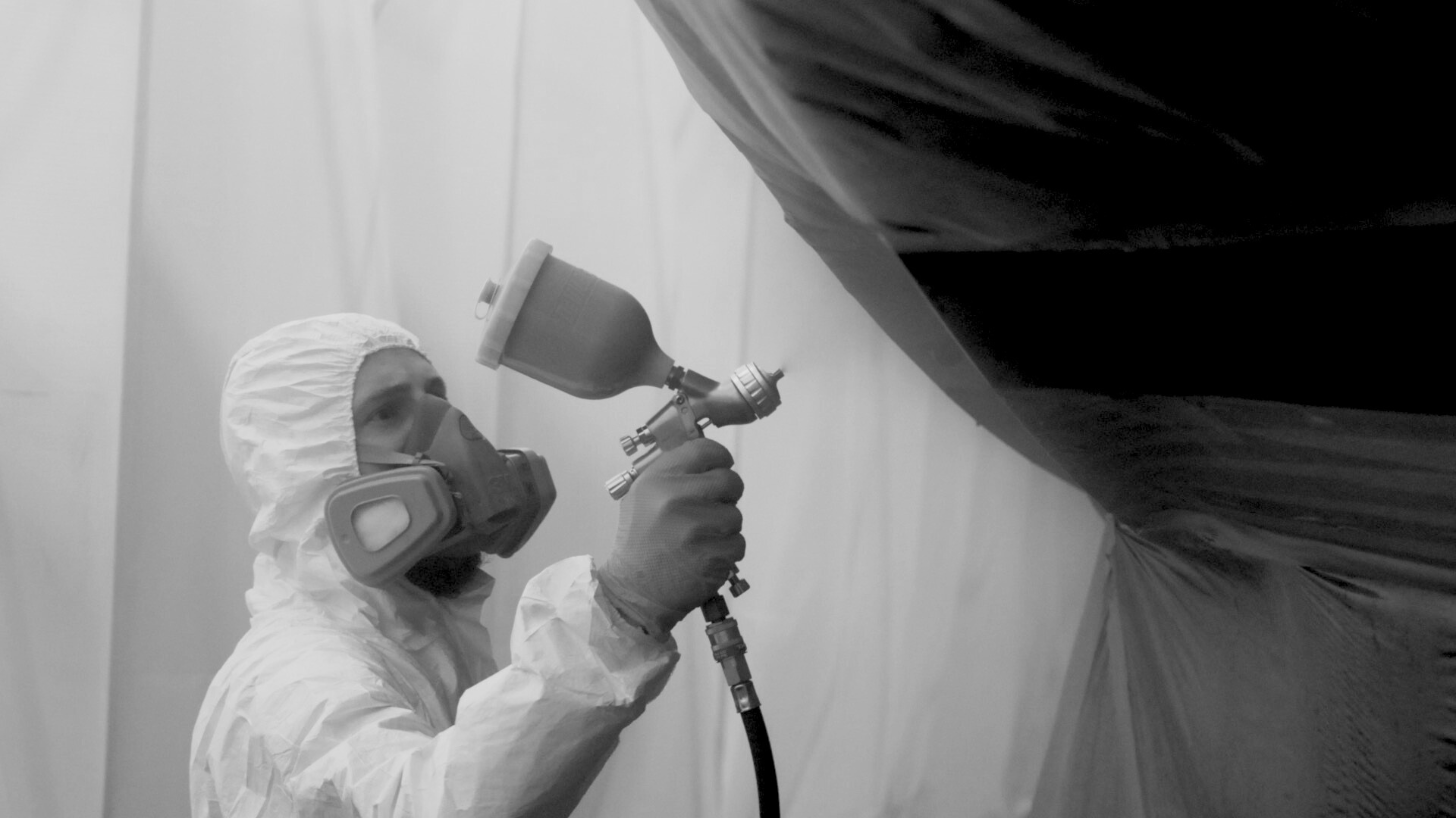 Operative using a spray gun inside a retractable spray booth during super yacht maintenance.