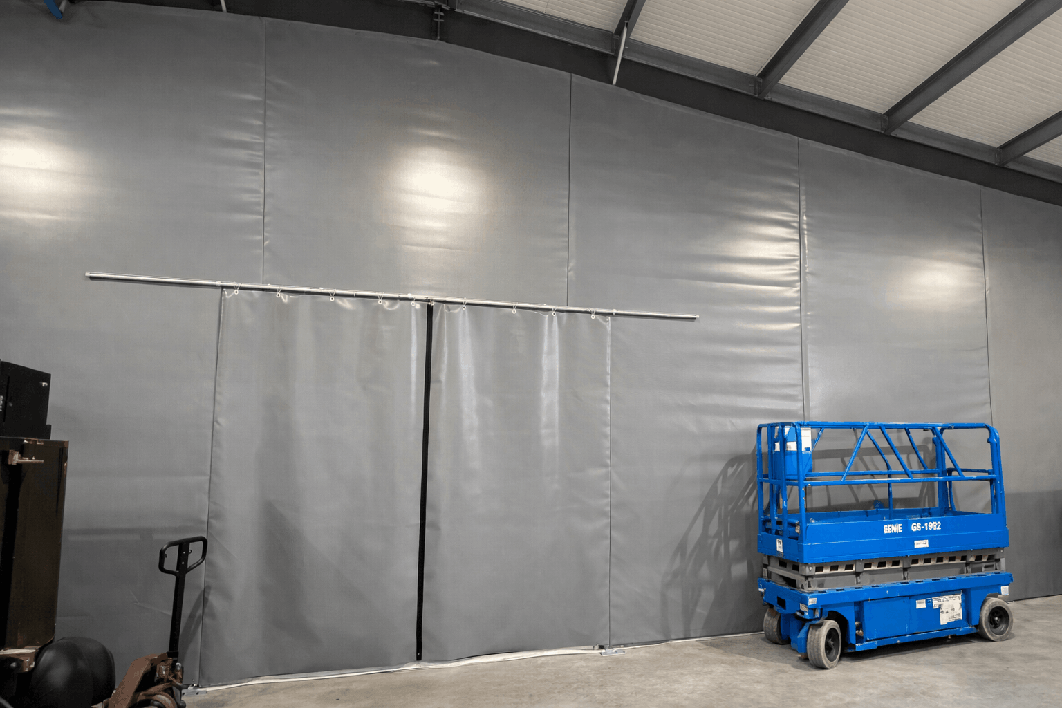 Industrial warehouse interior with a full-height grey PVC tension wall system, featuring a flexible sliding partition that creates a defined workspace while allowing easy access and adaptable space separation.