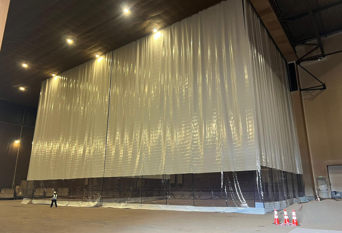 Large-scale warehouse partition installed by a manufacturer-installer, showing a floor-to-ceiling industrial curtain system precisely fitted within a high-bay warehouse to create a controlled, segregated workspace.